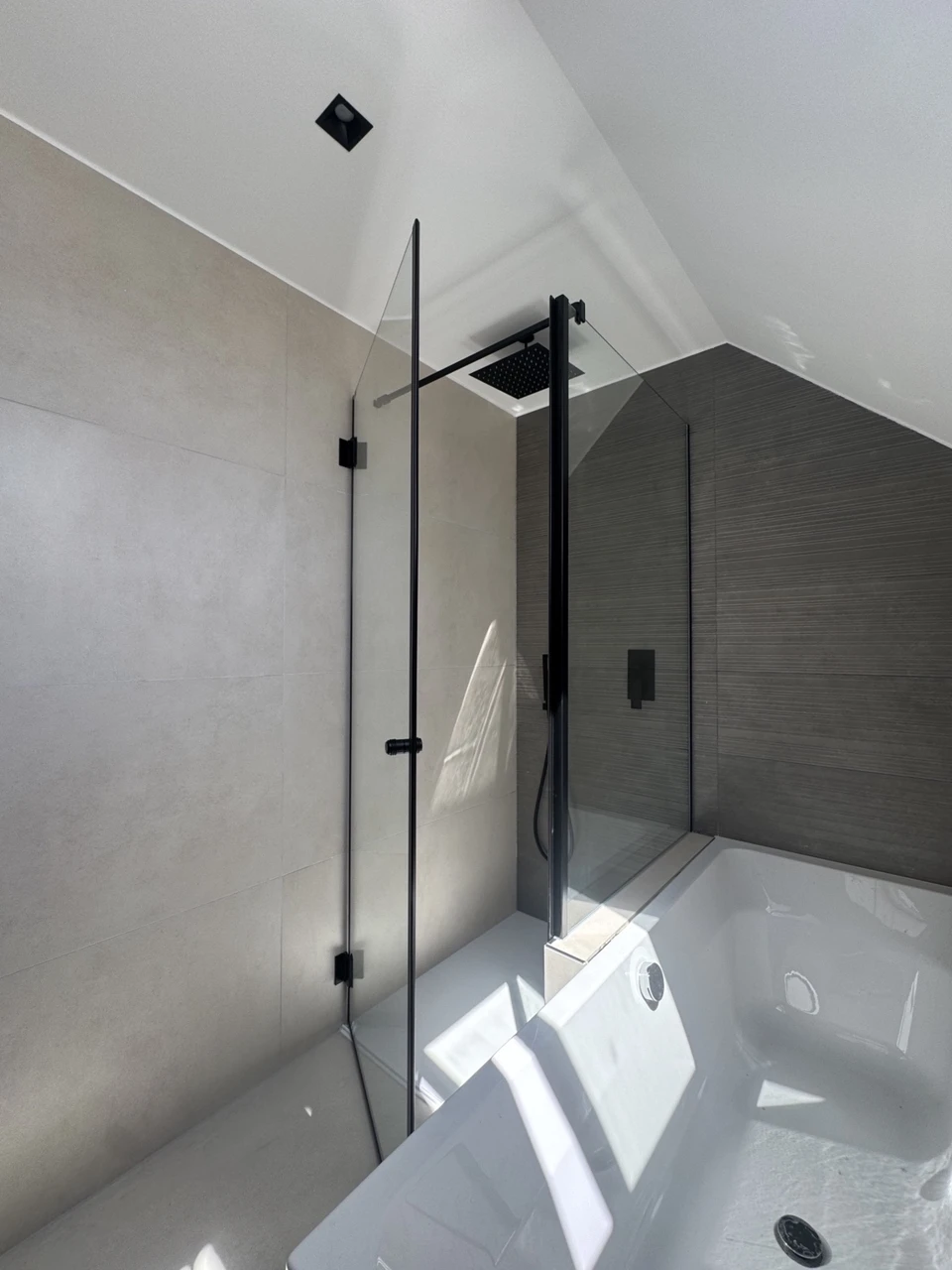 Eckdusche mit schwarzen Beschlägen neben einer weißen Badewanne